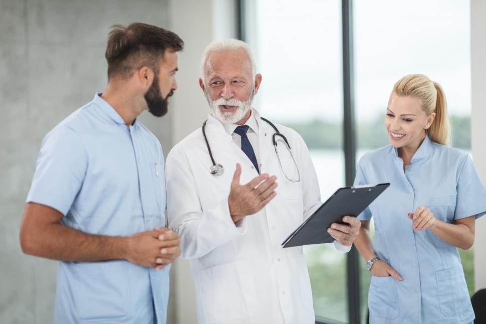 A smiling doctor wearing a white coat and stethoscope, with a heart and cross symbol representing care and compassion.